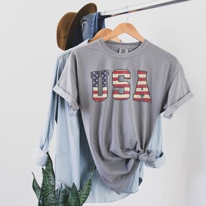 May include: A grey t-shirt with a vintage-style American flag graphic that reads "USA".