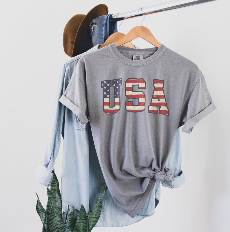 May include: A grey t-shirt with a vintage-style American flag graphic that reads "USA".