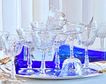 May include: A set of clear glass champagne coupes on a silver tray with a blue bottle of wine. The glasses are arranged in a circle with one glass upside down.