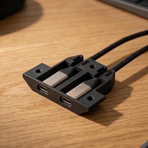 May include: A black dual-port USB-C mounting bracket featuring two integrated metallic USB-C connectors. The housing is constructed with a textured finish and includes two mounting holes on the sides for secure installation, with two black braided cables extending from the rear.