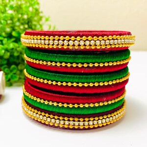 May include: A stack of red and green silk thread bangles with gold beads and clear rhinestones.