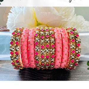 May include: A set of pink silk thread bangles with gold and clear rhinestone embellishments. The bangles are stacked together and have a pink and gold color scheme. The text "CUSTOMIZED" is visible on the left side of the image.
