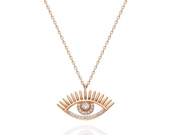 May include: Rose gold-toned necklace featuring an eye pendant. The pendant has a detailed eye design with a central, round, clear gemstone and surrounding clear gemstones. The necklace chain is delicate and the pendant is reflected below.