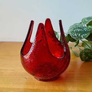 May include: A red glass vase with a textured surface and a unique, flower-like shape. The vase is perfect for displaying flowers or other decorative items.