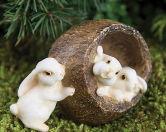May include: Three white ceramic bunnies, one peeking out of a brown hollowed-out log, a miniature figurine set for a fairy garden.