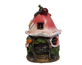 May include: A pink and white fairy house with a ladybug on top. The house has a small door and windows. It is made of resin and is perfect for a garden or fairy garden.