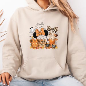 May include: Beige hoodie featuring a Halloween graphic. The design includes a Minnie Mouse figure with an orange bow, a pumpkin, a ghost, and the text "Literally just a girl". Also features a pumpkin spice latte and heart-shaped sunglasses.