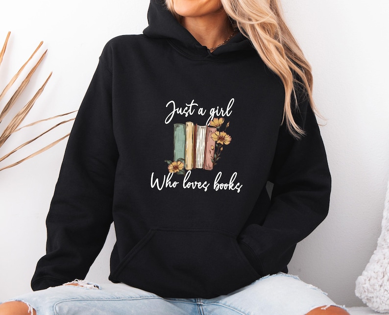 May include: Black hooded sweatshirt with a front pocket and the text "Just a girl Who loves books" in white script. The graphic features a stack of books in various colors with sunflowers.