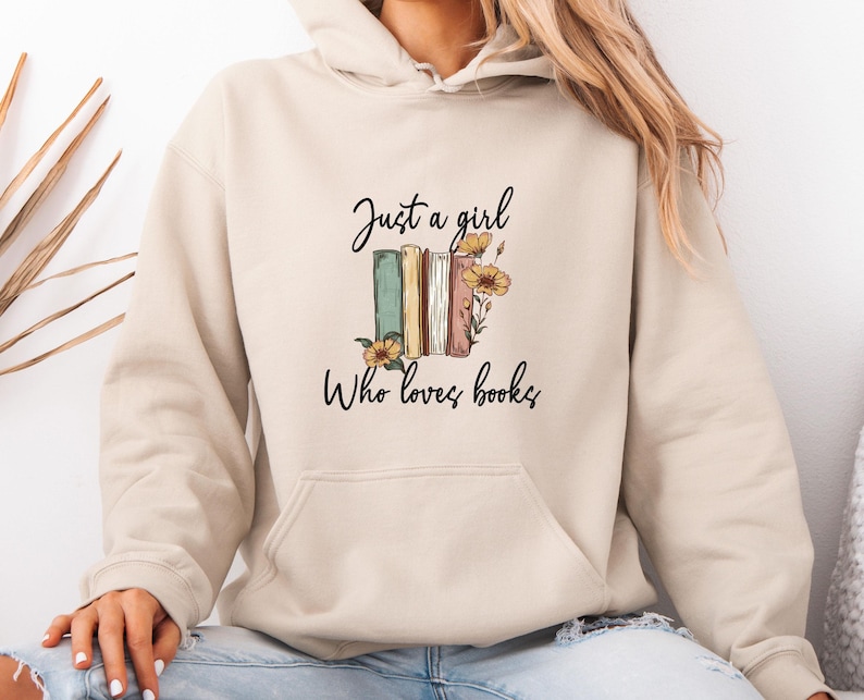 May include: Beige hoodie with a front pocket and a drawstring hood. The graphic on the front says "Just a girl Who loves books" with an illustration of books and flowers.