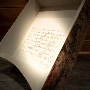 Puede incluir: Caja de madera en &aacute;ngulo con interior blanco y exterior con dise&ntilde;o decorativo. La caja tiene un dise&ntilde;o curvo y presenta texto manuscrito en el interior. El exterior tiene un dise&ntilde;o floral y bot&aacute;nico.