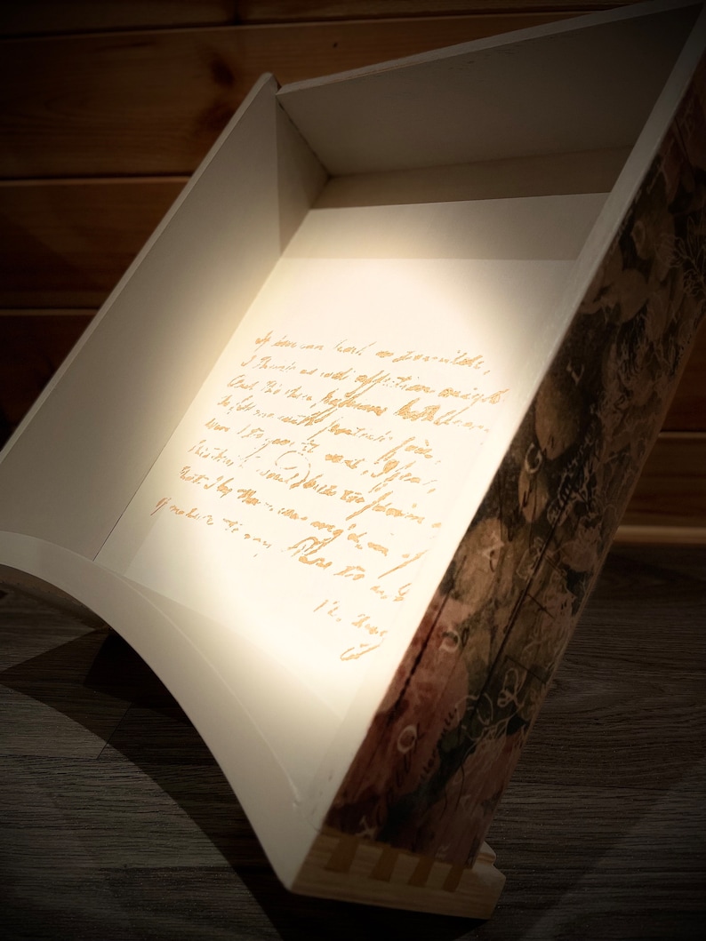 Puede incluir: Caja de madera en &aacute;ngulo con interior blanco y exterior con dise&ntilde;o decorativo. La caja tiene un dise&ntilde;o curvo y presenta texto manuscrito en el interior. El exterior tiene un dise&ntilde;o floral y bot&aacute;nico.