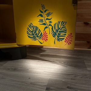 Pode incluir: Uma porta de arm&aacute;rio amarela com um desenho pintado de folhas verdes e flores vermelhas. A porta do arm&aacute;rio est&aacute; aberta e o interior do arm&aacute;rio &eacute; vis&iacute;vel.