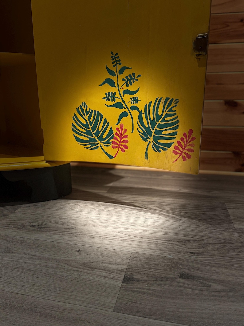 Pode incluir: Uma porta de arm&aacute;rio amarela com um desenho pintado de folhas verdes e flores vermelhas. A porta do arm&aacute;rio est&aacute; aberta e o interior do arm&aacute;rio &eacute; vis&iacute;vel.