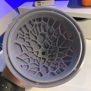 May include: A gray plastic diffuser with a geometric pattern. The diffuser has a circular shape and a small hole in the center.