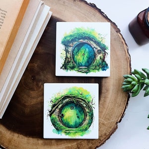 May include: Two square ceramic coasters with a watercolor painting of a green door with a round window. The door is surrounded by green vines and a stone wall. The background is a watercolor wash of green and yellow.