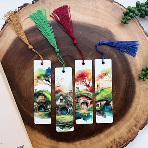 May include: Four rectangular bookmarks with colorful watercolor illustrations of hobbit homes. Each bookmark has a different colored tassel: gold, green, red, and blue. The bookmarks are displayed on a wooden surface next to an open book.