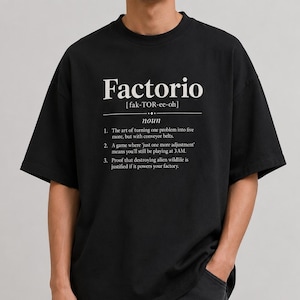 May include: Black t-shirt featuring the word "Factorio" in white, with its pronunciation and a definition. The definition includes three points about the game. The shirt is a crew neck and has short sleeves.