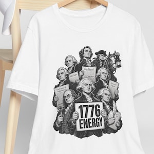 Könnte beinhalten: Weißes T-Shirt mit einer Schwarz-Weiß-Grafik historischer Persönlichkeiten, die Dokumente halten. Die Grafik enthält den Text "1776 ENERGY". Eine weiße Baseballkappe hängt an einem Holzstuhl.