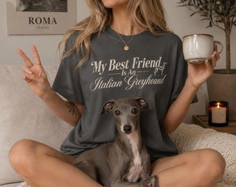 以下が含まれることがあります： 「My Best Friend Is An Italian Greyhound」という白い文字と犬のシルエットがプリントされたダークグレーのTシャツ。半袖でクルーネックのデザインで、無地の生地にグラフィックが施されています。