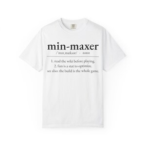 May include: A white short-sleeved t-shirt featuring black text that defines the word min-maxer. The graphic includes a phonetic pronunciation, the label noun, and two numbered points: 1. read the wiki before playing. 2. fun is a stat to optimize.