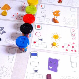 Peut inclure: Un ensemble de contenants de pâte à modeler colorés avec différentes formes et des nombres. Les contenants sont étiquetés avec les nombres 4, 6 et 10. Il y a aussi des formes de pâte à modeler, y compris des cœurs, des carrés et des cercles.