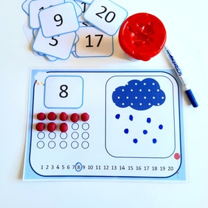 Peut inclure: Un tapis d'apprentissage bleu et blanc avec un nuage et des gouttes de pluie. Le tapis comporte une ligne de nombres de 1 à 20 et une section pour compter avec des compteurs rouges. Le nombre 8 est écrit dans une case en haut du tapis.