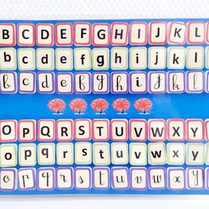 May include: A blue and white alphabet chart with three red trees. The chart has three rows of letters, with the first row in uppercase, the second row in lowercase, and the third row in cursive lowercase.