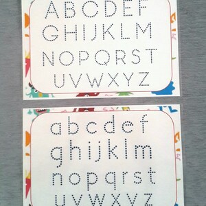 May include: Two white cards with a colorful border. The top card has the alphabet in uppercase letters, with each letter outlined in dotted lines. The bottom card has the alphabet in lowercase letters, with each letter outlined in dotted lines.