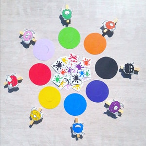 May include: A colorful game with a variety of monster characters, colorful circles, and small colorful stickers. The game is laid out on a light wood surface.