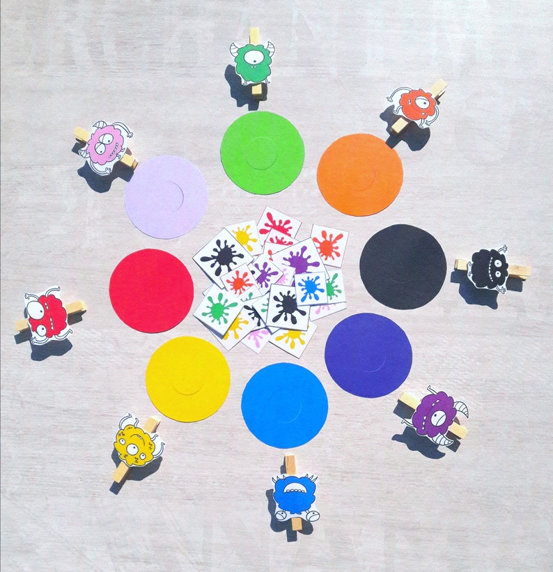 May include: A colorful game with a variety of monster characters, colorful circles, and small colorful stickers. The game is laid out on a light wood surface.