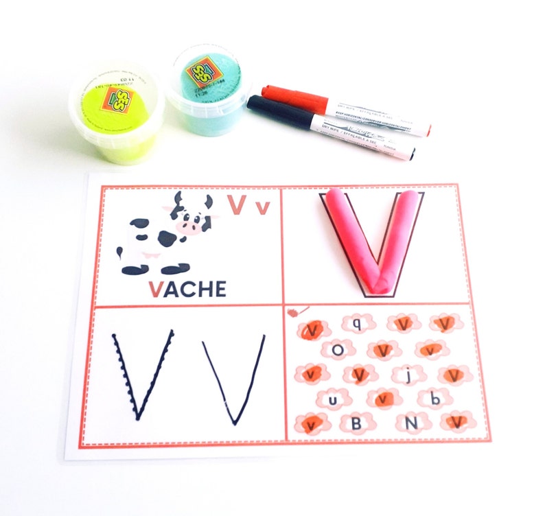 May include: A white card with a red border and the letter V printed on it. The letter V is also formed with pink playdough. There are several other Vs printed on the card, as well as the word VACHE.