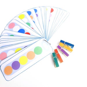 Puede incluir: Un conjunto de tarjetas coloridas con c&iacute;rculos en ellas, dispuestas en forma de abanico. Las tarjetas se utilizan para una actividad de coincidencia de colores. Tambi&eacute;n hay pinzas para la ropa de colores.