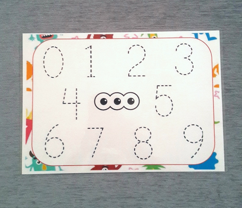May include: A white sheet of paper with a red border and a dotted line outline of the numbers 0 through 9. There are three black circles in the center of the sheet.
