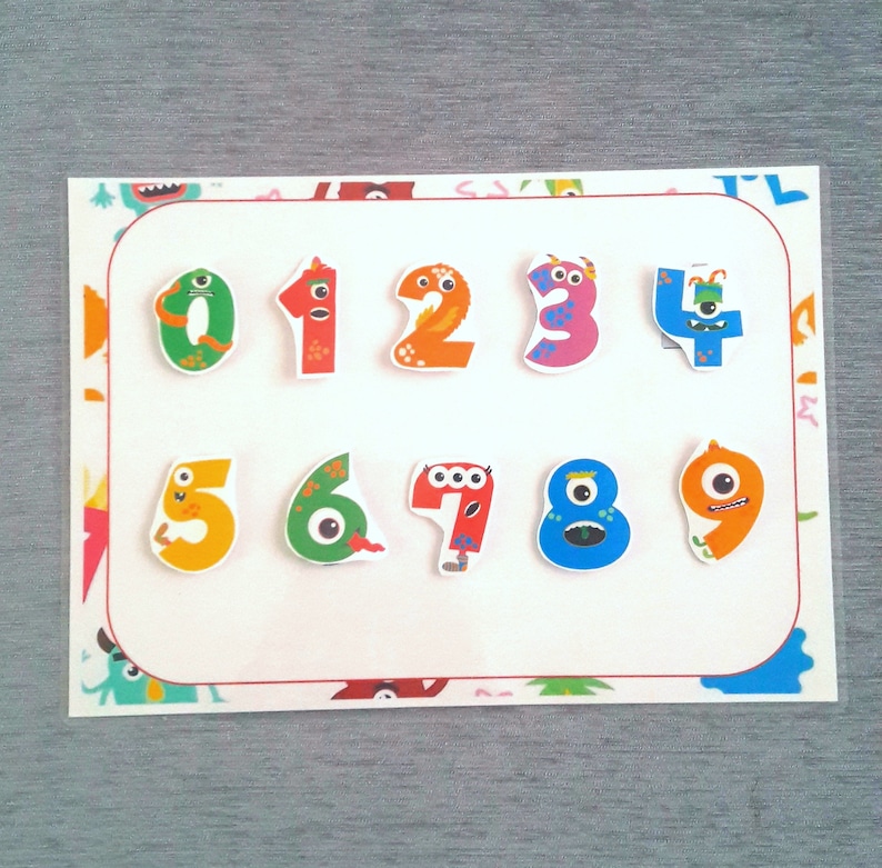 May include: A white card with a red border features colorful monster-shaped numbers from 1 to 9. Each number has a different color and a unique monster face.