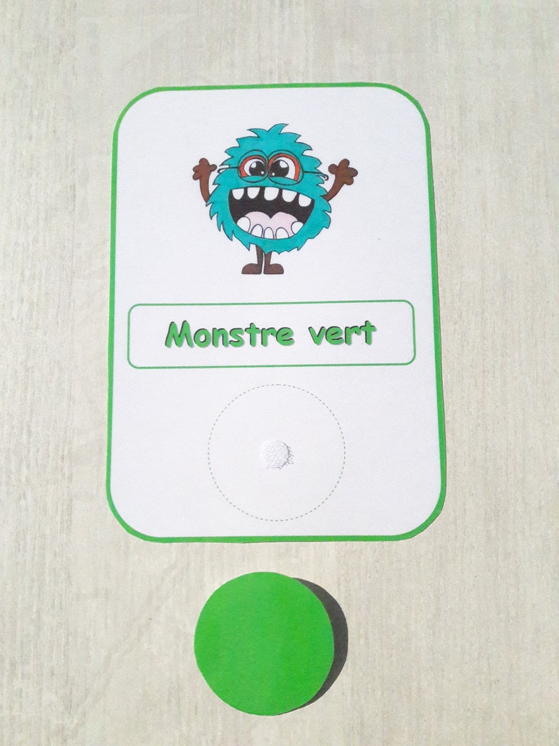 May include: A green monster with a toothy grin and glasses is on a white card with the text "Monstre vert". A green circle is below the card.
