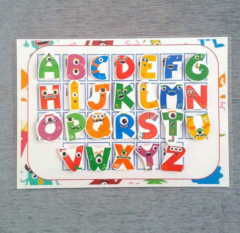 May include: A colorful alphabet chart with each letter represented by a cartoon monster. The letters are arranged in a grid with a white background and a colorful border.
