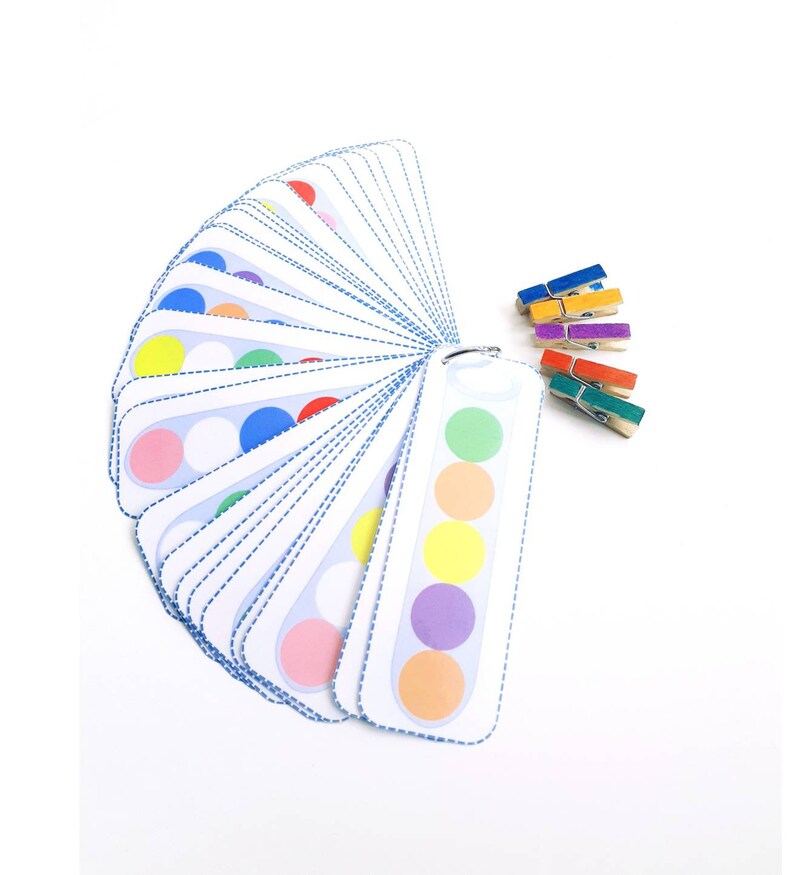 Puede incluir: Un juego de tarjetas de coincidencia de colores con una variedad de colores, incluyendo rojo, naranja, amarillo, verde, azul, morado y rosa. Las tarjetas est&aacute;n dispuestas en forma de abanico y se mantienen unidas por un anillo de metal. Tambi&eacute;n hay un juego de pinzas para la ropa de colores.