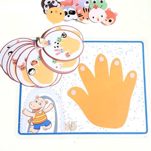May include: A colorful learning game with a hand-shaped board and animal-themed cards. The board has a yellow hand with five fingers and a blue border. The cards feature different animals, including a panda, a raccoon, a tiger, a chicken, and a squirrel. The cards are arranged in a circle around the hand.