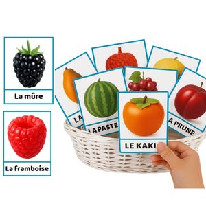 K&ouml;nnte beinhalten: Ein wei&szlig;er Weidenkorb enth&auml;lt Obstkarten, darunter eine Brombeere, eine Himbeere, eine Papaya, eine Wassermelone, Trauben, eine Kaki und eine Pflaume. Die Karten haben blaue R&auml;nder und Obstnamen auf Franz&ouml;sisch. Eine Hand h&auml;lt eine Karte mit der Aufschrift "LE KAKI".
