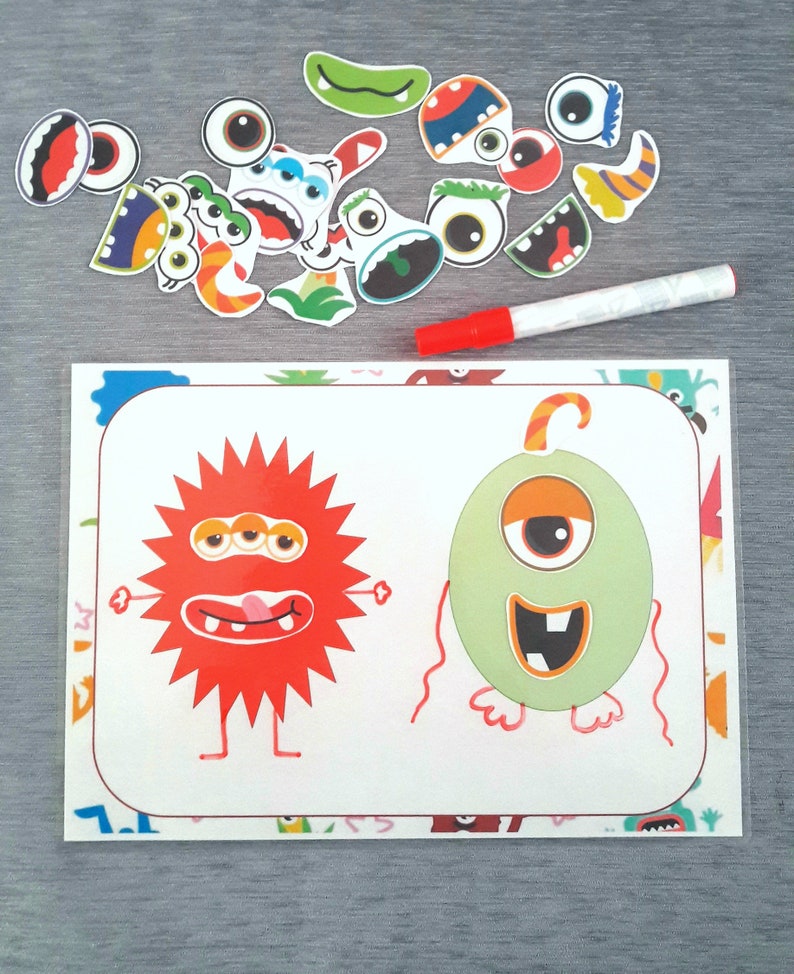 May include: A white card with two cartoon monsters on it. The monster on the left is red with three eyes and a tongue sticking out. The monster on the right is green with one eye and a toothy grin. There are colorful monster stickers scattered around the card.
