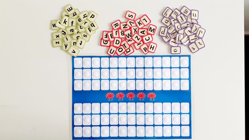 May include: A blue game board with white circles and three red trees. There are three piles of letter tiles in different colours: green, red, and purple.