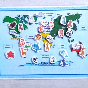 May include: A colorful world map with animal stickers representing different continents. The map includes the names of the continents and oceans in French. The animals include a giraffe, zebra, tiger, lion, kangaroo, penguin, polar bear, octopus, dolphin, and more.
