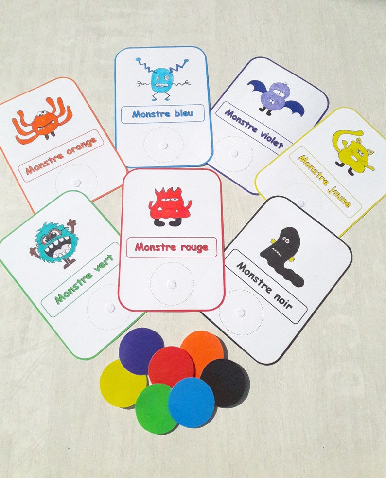 May include: A set of six colorful monster cards with matching colored circles. Each card features a different monster with a French word describing the color of the monster. The words are "Monstre orange", "Monstre bleu", "Monstre vert", "Monstre rouge", "Monstre violet", and "Monstre jaune".