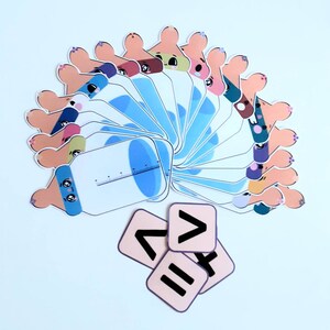 May include: A set of 16 baby bottle shaped cards with different coloured faces and a set of 4 cards with maths symbols: greater than, less than, equals, and plus.