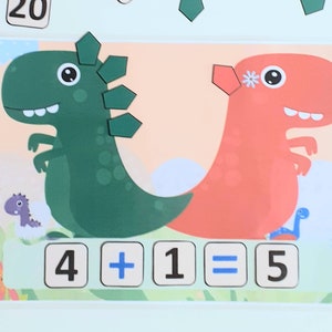 Op de afbeelding: Een groene en rode dinosauruspuzzel met een wiskundige vergelijking: 4 + 1 = 5. De dinosaurussen hebben een bloem en stekels op hun kop.