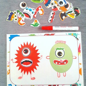 May include: A white card with two monster illustrations. The monster on the left is red with a star shape and the monster on the right is green and oval shaped. Both monsters have eyes, mouths, and arms. There are colorful monster stickers around the card.