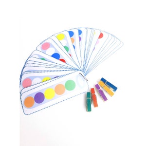Puede incluir: Un juego de tarjetas de coincidencia de colores con una variedad de c&iacute;rculos de colores. Las tarjetas est&aacute;n dispuestas en forma de abanico y se mantienen unidas con un anillo de metal. Tambi&eacute;n hay cinco pinzas para la ropa de colores.