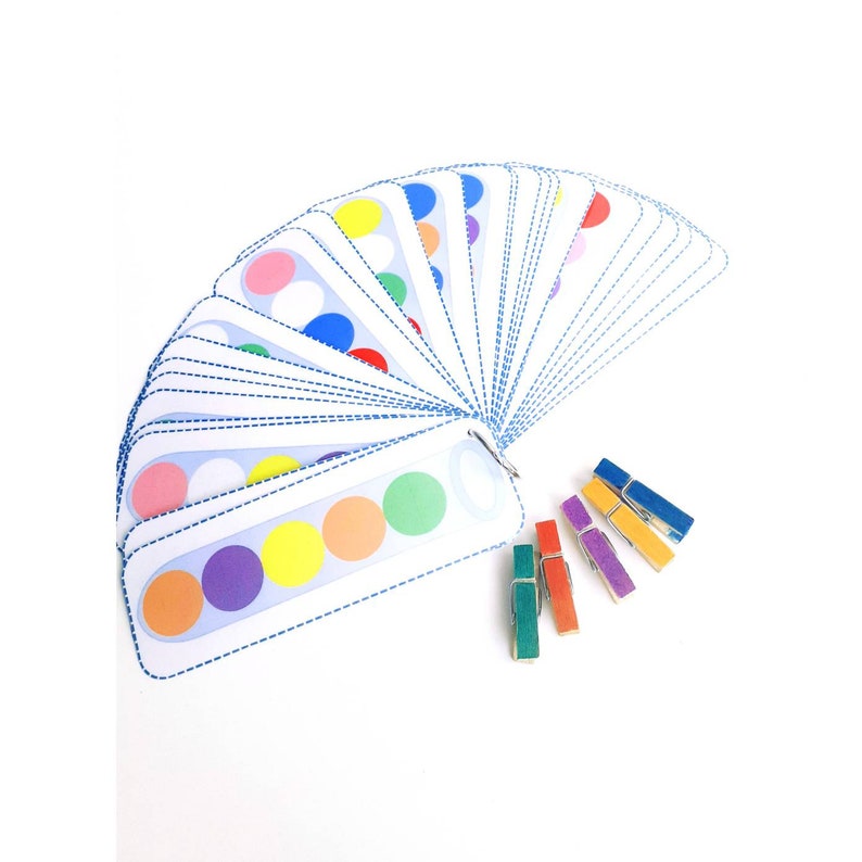 Puede incluir: Un juego de tarjetas de coincidencia de colores con una variedad de c&iacute;rculos de colores. Las tarjetas est&aacute;n dispuestas en forma de abanico y se mantienen unidas con un anillo de metal. Tambi&eacute;n hay cinco pinzas para la ropa de colores.
