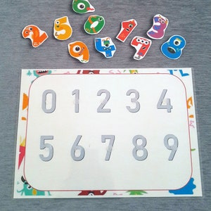 May include: A white board with the numbers 0-9 printed in gray. There are ten colorful monster-shaped pieces with numbers 0-9 printed on them.