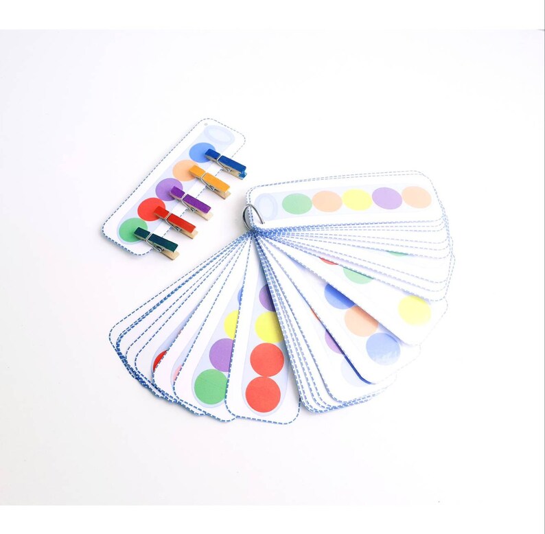 Puede incluir: Un conjunto de tarjetas circulares de colores con un juego a juego de pinzas para la ropa. Las tarjetas est&aacute;n dispuestas en forma de abanico y tienen un borde punteado azul. Las pinzas para la ropa son rojas, naranjas, amarillas, verdes, azules y moradas.